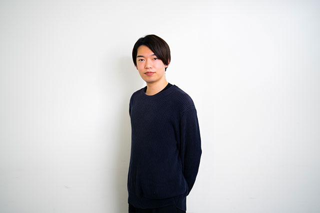白壁をバックに立ち、ポーズを決めるKOHEI