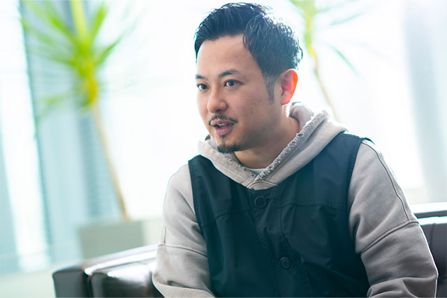 グレーのパーカーに紺色のベストを着たTAKAYUKI