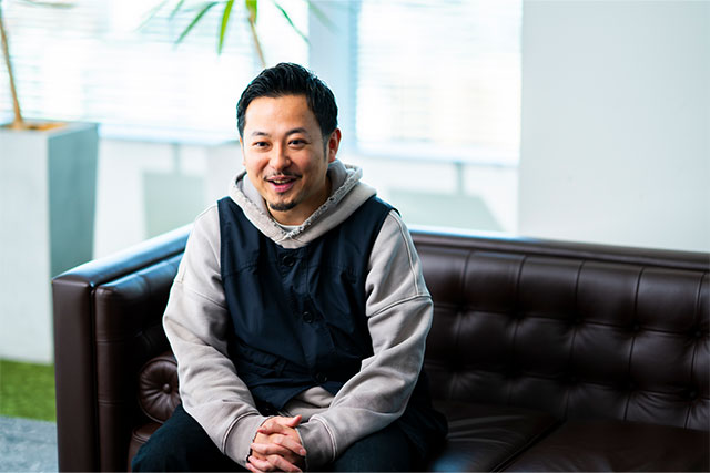手を組み、笑顔で話すTAKAYUKI