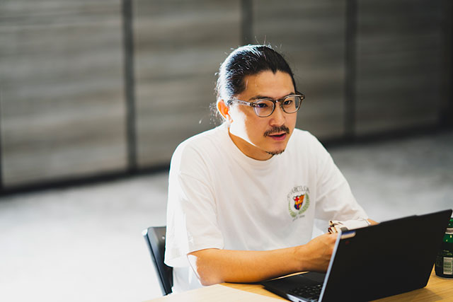 白いTシャツを着て後ろで髪を結い、眼鏡をかけた北瀨雄大